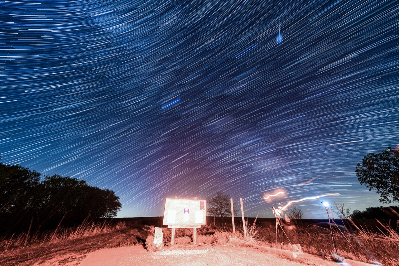 Star trails arcing over a prairie trailhead sign in Illinois.