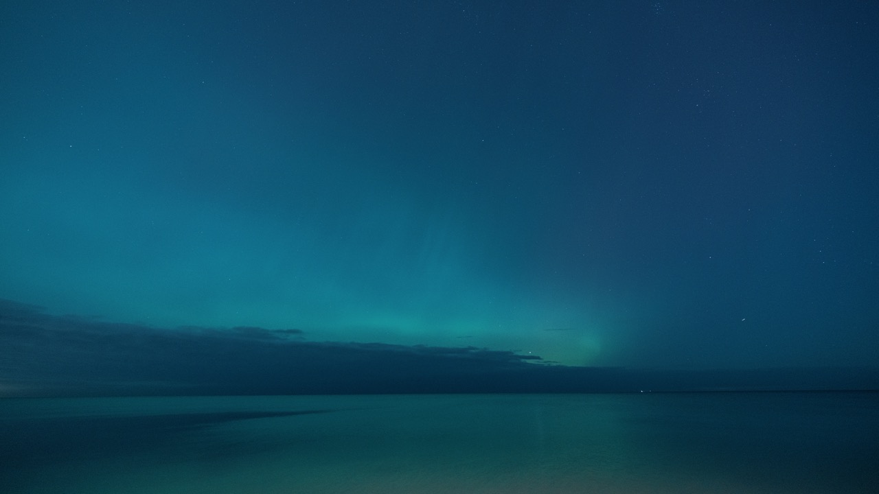 Soft teal aurora over calm Lake Michigan waters.